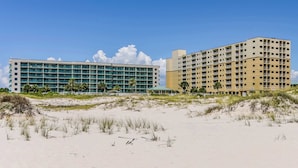 A beachfront hotel with multiple floors, a flat roof, and a sandy beach in the foreground. - Spacious and inviting seaside condo with shared pools, sauna (Fort Morgan)