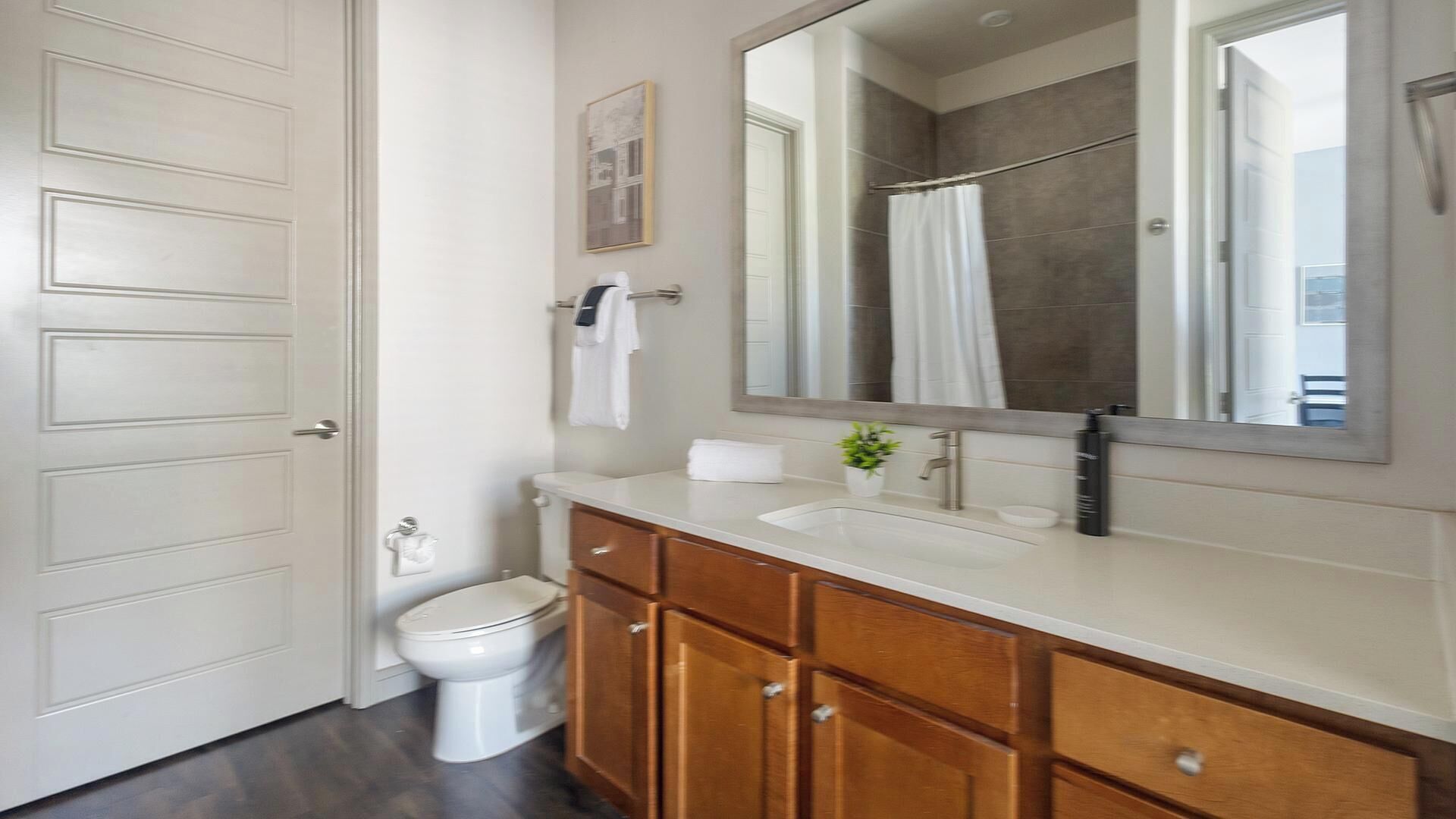 A bathroom with a white toilet, wooden cabinets, a white sink, a large mirror, and a shower curtain.