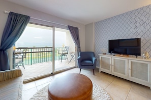 A living room with a sofa, ottoman, TV, and a patterned wall. - Waterfront condo with shared pool & hot tub - walk to dining & beach (Fort Morgan)