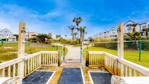Um deck de madeira que leva a um portão com vista para prédios residenciais e palmeiras.