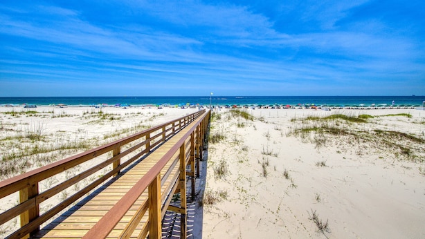 A wooden boardwalk leading to a beach with sand dunes and a clear blue sky. - Condo Steps from the Sand with Balcony, Resort Pools, Central AC, & WiFi (Fort Morgan)