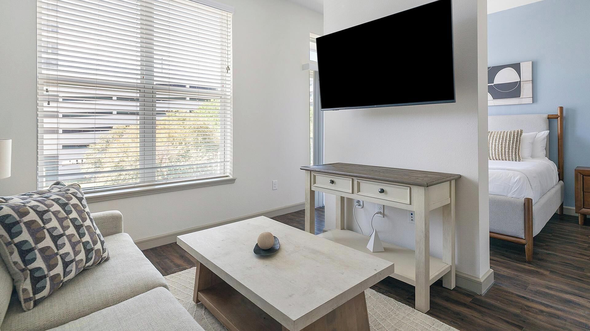 Ein modernes Zimmer mit einer Couch, einem Couchtisch, einem an der Wand befestigten Fernseher und einem Bett.