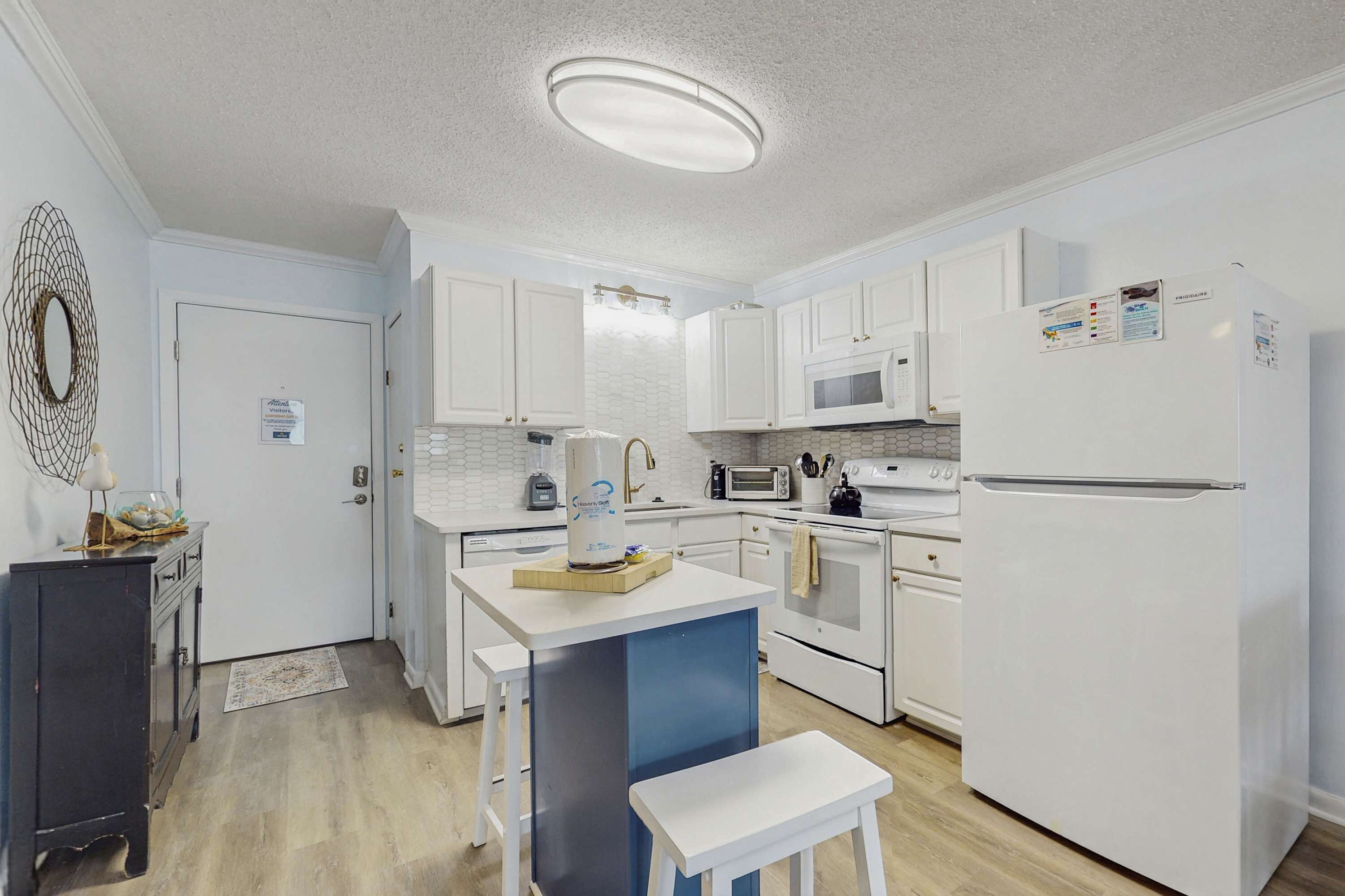 A modern kitchen with white cabinets, a built-in microwave, a refrigerator, and a small island with stools.