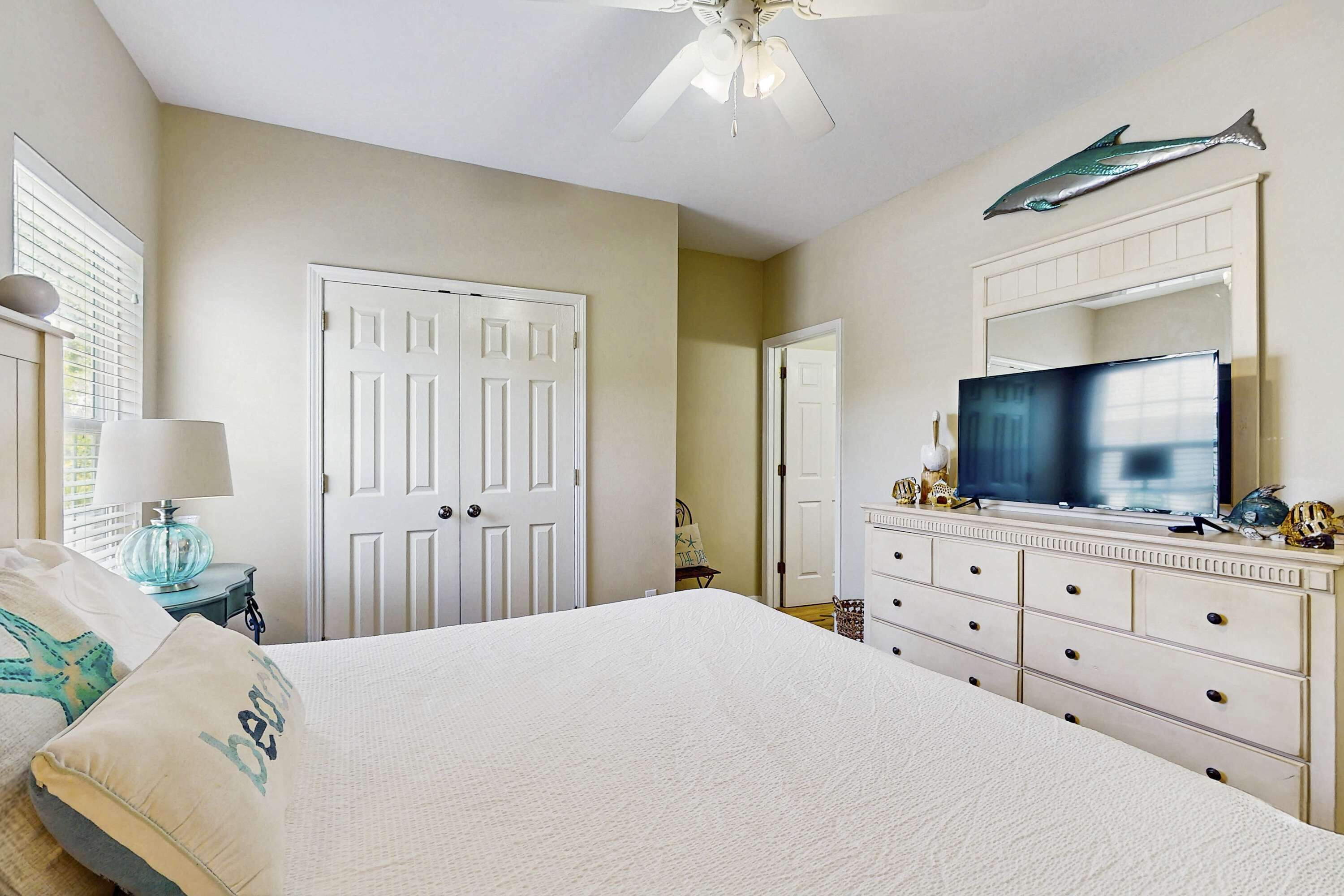 Une chambre à coucher comprenant un lit, une commode, un téléviseur et un ventilateur de plafond.