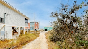 A coastal road with buildings, including a white house with a porch and a red building in the distance. - Beachfront home with furnished deck, great location, & WiFi (Fort Morgan)