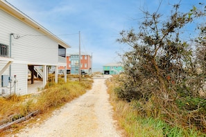 A coastal road with buildings, including a white house with a porch and a red building in the distance. - Beachfront home with furnished deck, great location, & WiFi (Fort Morgan)