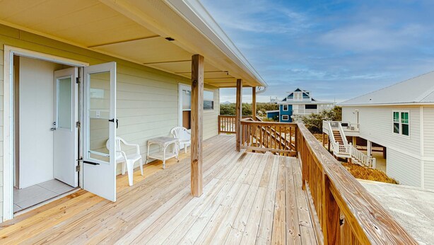 A wooden deck with a covered porch, white chairs, and a view of neighboring houses. - Beachfront home with furnished deck, great location, & WiFi (Fort Morgan)