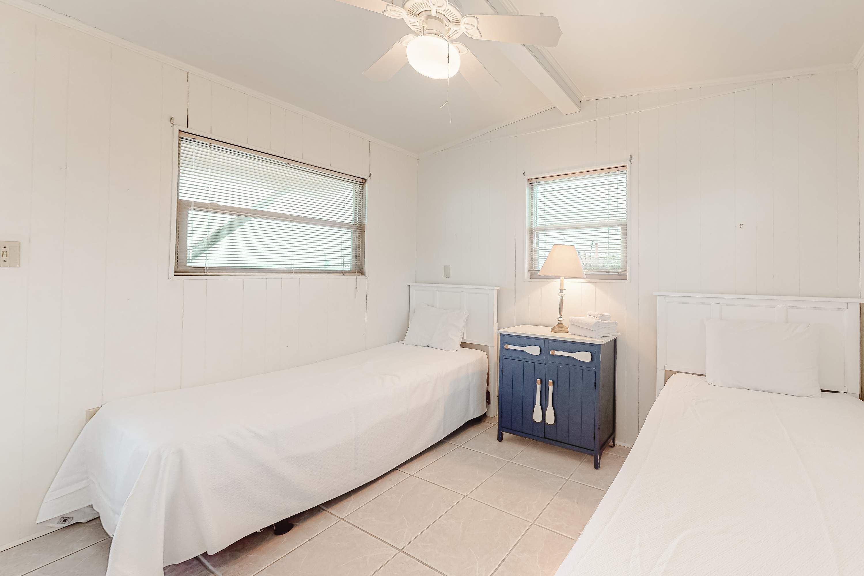 A room with two beds, a small cabinet, and a ceiling fan.