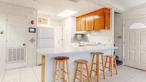 A kitchen with wooden cabinets, a white countertop, and three stools. - Beachfront home with furnished deck, great location, & WiFi (Fort Morgan)