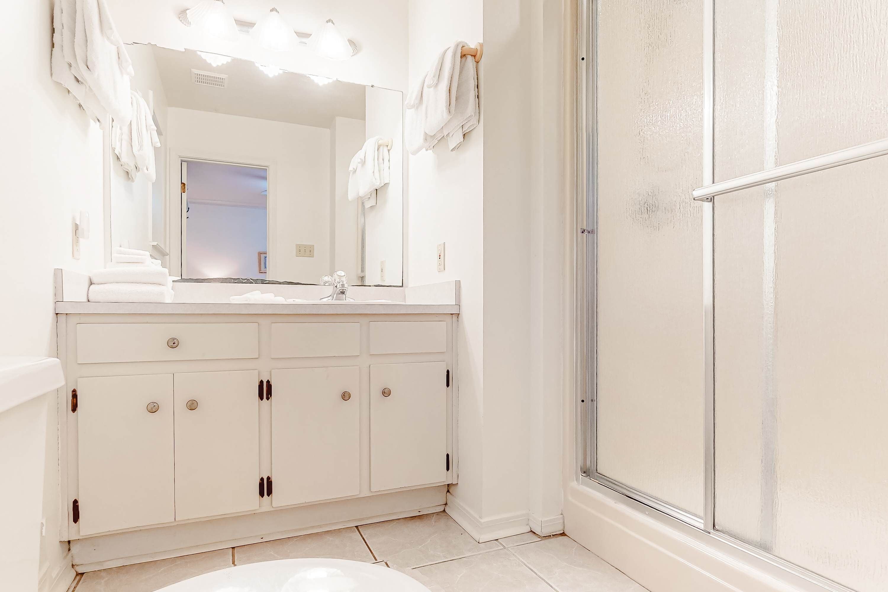 A bathroom with a white vanity, a mirror, a shower, and a door leading to another room.
