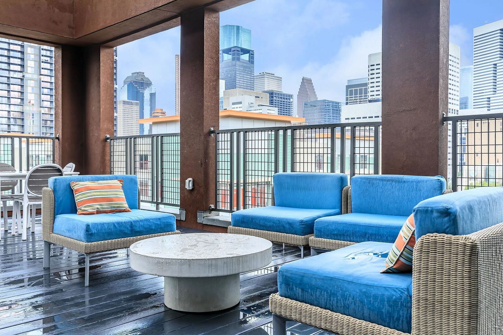 A rooftop terrace with wicker furniture, a round table, and a city skyline view.
