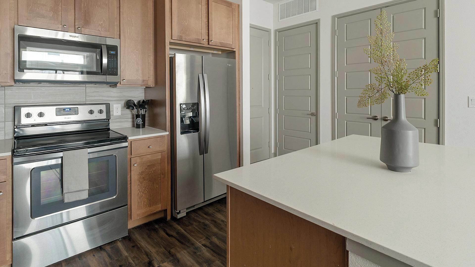 A modern kitchen with stainless steel appliances, wooden cabinets, and a white countertop.