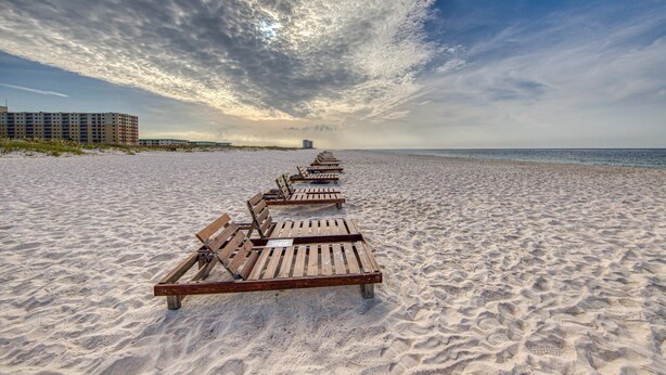 Une plage avec des chaises longues en bois alignées en rangées, une plage de sable et un bâtiment situé au loin.