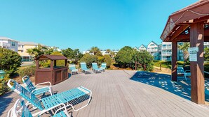 Une terrasse en bois avec des chaises longues et un belvédère, d’où l’on a vue sur une piscine et des immeubles d’habitation.