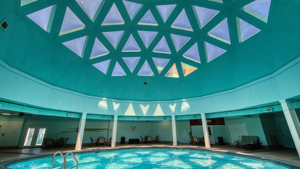 En inomhuspool med ett geometriskt utformat tak, flera sittområden och fri sikt över poolen.