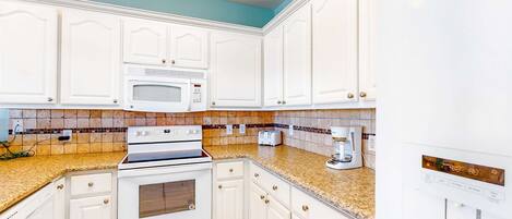 A kitchen with white cabinets, a microwave, a stove, and a coffee maker.