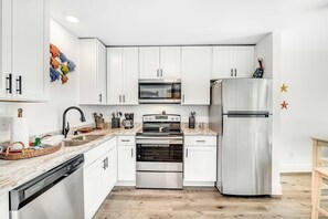 A modern kitchen with white cabinets, stainless steel appliances, and a wooden floor. - Condo near the beach with shared, heated pool and tennis (Fort Morgan)