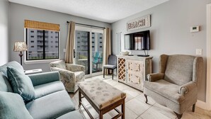 Una sala de estar con sofá, sillón, reposapiés, televisor y aparador.