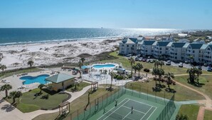 Et resort med strand, swimmingpool, tennisbaner og en bygning med grønt tag.