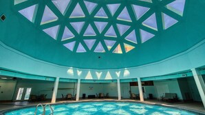 An indoor swimming pool with a geometric glass ceiling, multiple lounge areas, and a clear view of the pool. - Gulf view home with two-level deck, beach access & shared pools, hot tub, gym (Fort Morgan)