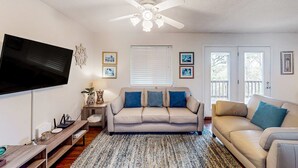 A living room with a flat-screen TV, a ceiling fan, a sofa, a coffee table, and a rug. - Gulf view home with two-level deck, beach access & shared pools, hot tub, gym (Fort Morgan)