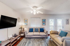 A living room with a flat-screen TV, a ceiling fan, a sofa, a coffee table, and a rug. - Gulf view home with two-level deck, beach access & shared pools, hot tub, gym (Fort Morgan)