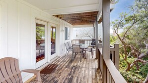 A covered deck with a table and chairs, a wooden floor, and a white exterior wall. - Gulf view home with two-level deck, beach access & shared pools, hot tub, gym (Fort Morgan)