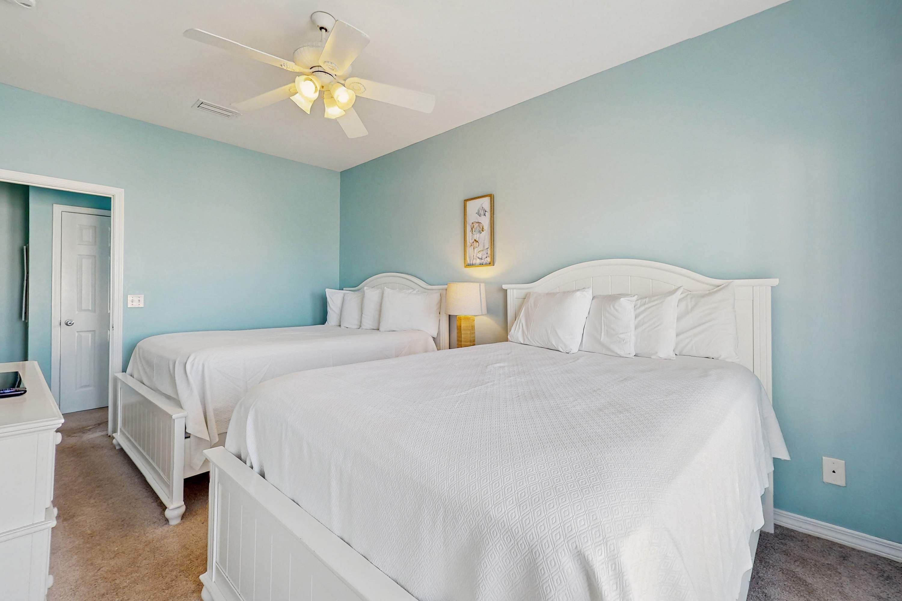 A bedroom with two beds, a ceiling fan, a door, and a nightstand.