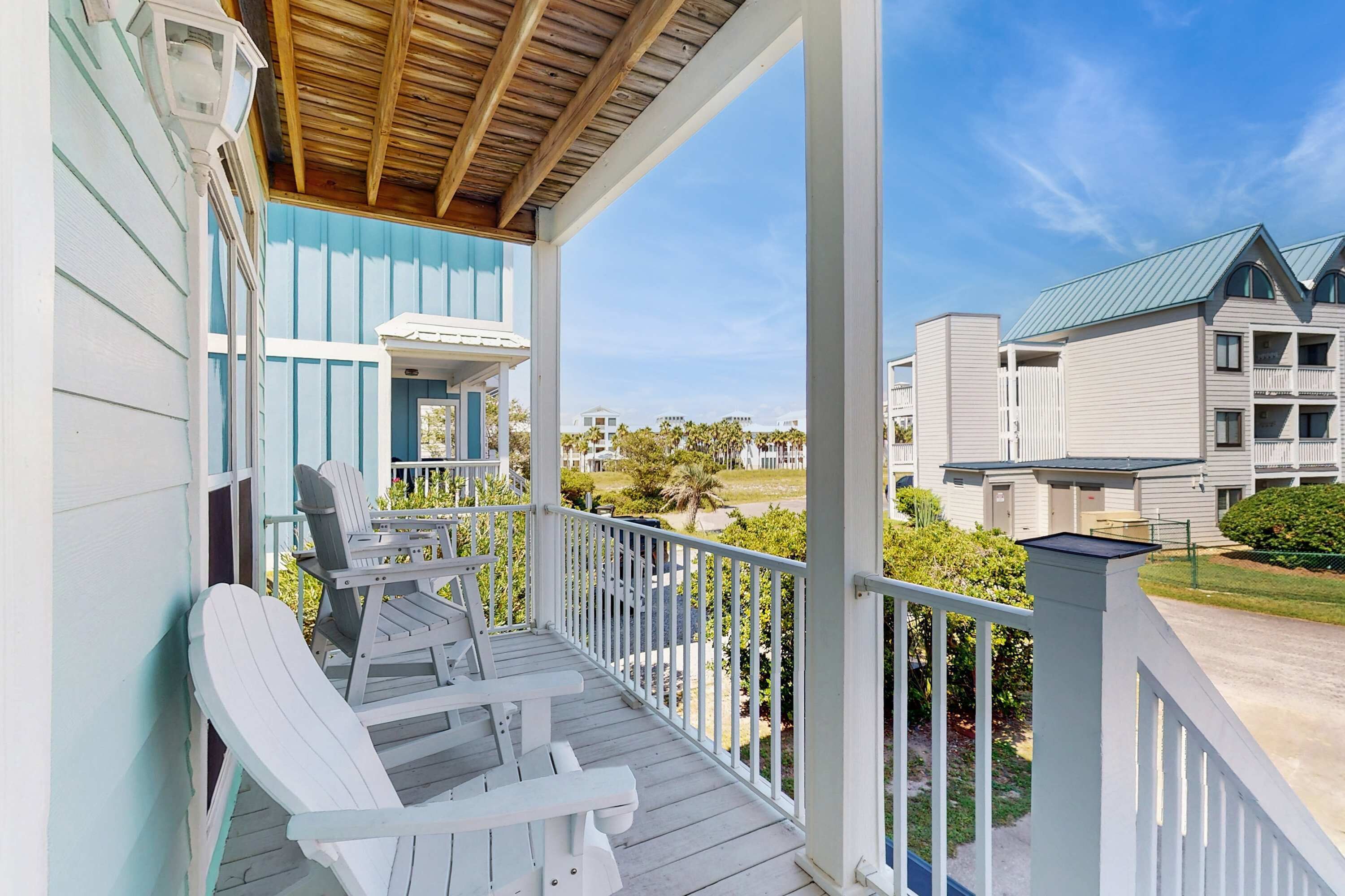 A covered porch with Adirondack chairs, a wooden ceiling, and a view of a building with a green roof.