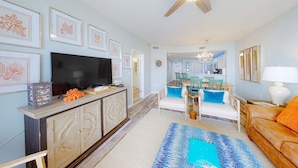 A living room with a TV, sofa, and dining area. - Gulffront Condo W Furnished Deck, Beach Access, Fast WiFi & Shared Pool Hot Tub (Fort Morgan)