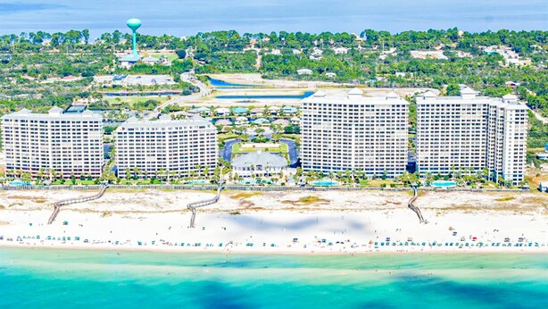 A coastal hotel with multiple high-rise buildings, a beach, and a water tower. - Gulffront Condo W Furnished Deck, Beach Access, Fast WiFi & Shared Pool Hot Tub (Fort Morgan)