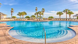 A swimming pool with a curved edge, palm trees, and a clear blue sky. - Gulffront Condo W Furnished Deck, Beach Access, Fast WiFi & Shared Pool Hot Tub (Fort Morgan)