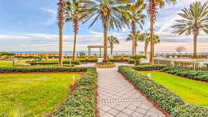 A pathway flanked by palm trees and well-manicured lawns, leading to a gazebo. - Gulffront Condo W Furnished Deck, Beach Access, Fast WiFi & Shared Pool Hot Tub (Fort Morgan)