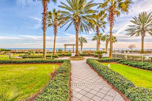 A pathway flanked by palm trees and well-manicured lawns, leading to a gazebo. - Gulffront Condo W Furnished Deck, Beach Access, Fast WiFi & Shared Pool Hot Tub (Fort Morgan)
