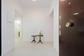 A hallway with a wooden door, two small tables with plants, and a white wall with a framed picture. - Welcome in Vatican vista apartment with Balcony (Roma)