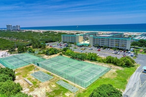 A hotel with multiple tennis courts, a parking lot, and a view of the beach and ocean.