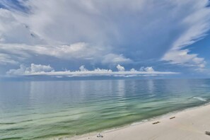 Een strand met helder water, een zandstrand en een lichtbewolkte lucht.