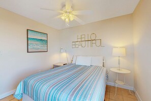 Ein Schlafzimmer mit einem Bett, einem Deckenventilator, einer Wandlampe, einem kleinen Nachttisch und einem gerahmten Bild.