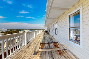 Eine Holzterrasse mit Geländer, mit Blick auf ein Gewässer und Gebäude.