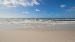 En strand med bølger, klar himmel og sandet bredde.