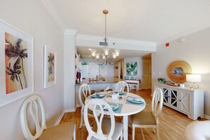 A dining area with a round table, white chairs, a chandelier, and a white cabinet with a round mirror. - Waterfront condo with indoor & outdoor pools, hot tubs, & on-site restaurants (Fort Morgan)