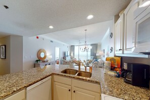A kitchen with granite countertops, white cabinetry, a coffee maker, and a dining area with a chandelier. - Waterfront condo with indoor & outdoor pools, hot tubs, & on-site restaurants (Fort Morgan)