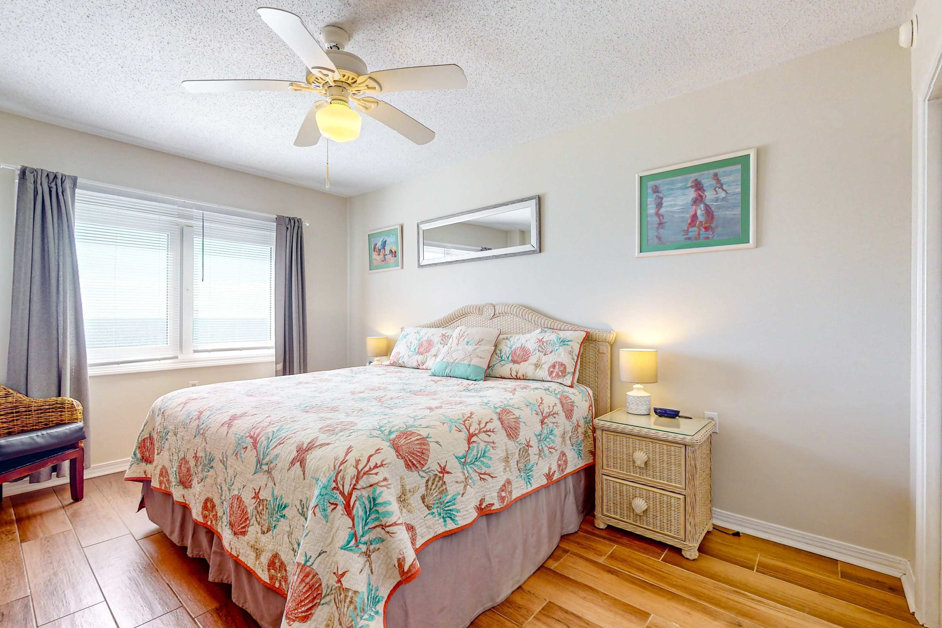 Quarto com cama, mesa de cabeceira, ventilador de teto, janela com cortinas e obras de arte na parede.