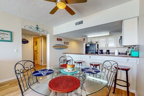 A dining area with a glass table, metal chairs, and a ceiling fan. - Tropical Winds beachfront beauty with pool, balcony, grills - close to beach (Gulf Shores)