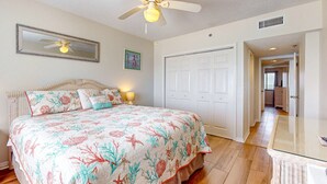 Ein Schlafzimmer mit Bett, Deckenventilator, einer Tür und einem zur nächsten Kammer führenden Gang.