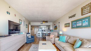 Ein Wohnzimmer mit Fernseher, einer Couch, einem Couchtisch und einer Küche im Hintergrund.