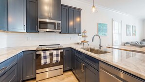 A modern kitchen with dark cabinets, stainless steel appliances, a marble countertop, and a pendant light. - Coastal dog-friendly gem near beach & town with pool, balcony, & central AC (Gulf Shores)