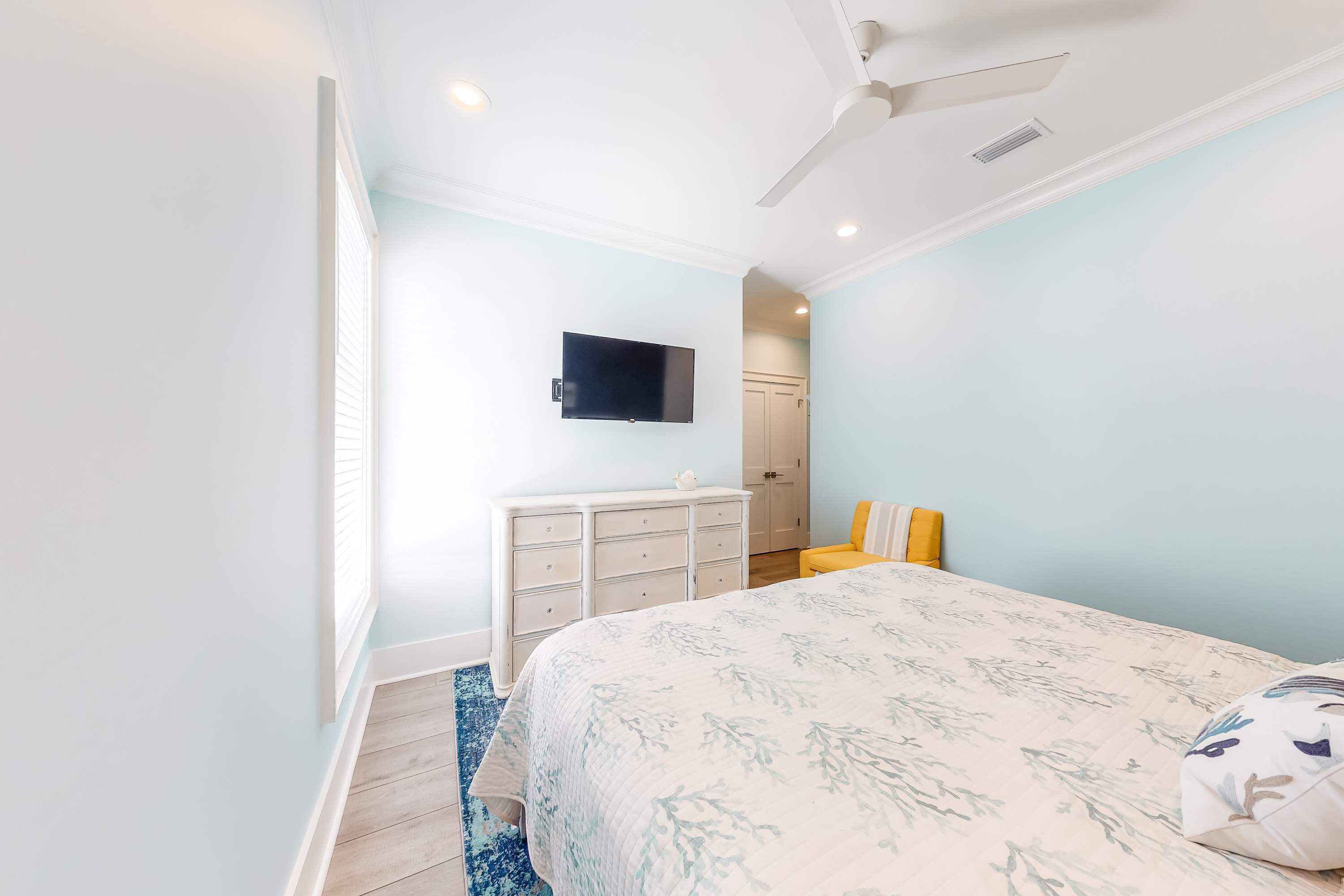 Un dormitorio con cama, cómoda, televisor y ventilador de techo.