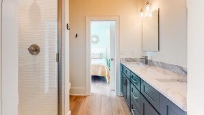 A bathroom with a glass shower enclosure, a sink with a marble countertop, and a mirror with lights. - Coastal dog-friendly gem near beach & town with pool, balcony, & central AC (Gulf Shores)