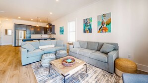 A modern living room with two sofas, a coffee table, and a kitchen in the background. - Coastal dog-friendly gem near beach & town with pool, balcony, & central AC (Gulf Shores)